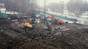 Gravemaskiner og arbeidere i stor byggegrop med sprengstein og masser