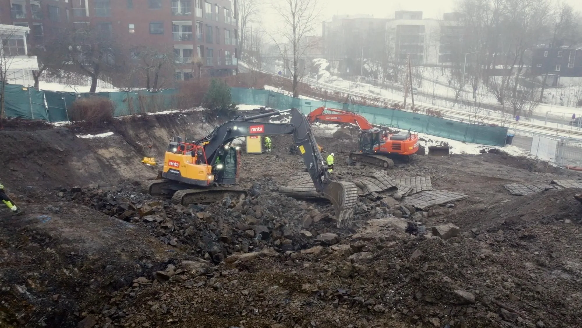 Gravemaskiner og arbeidere i stor byggegrop med sprengstein og masser