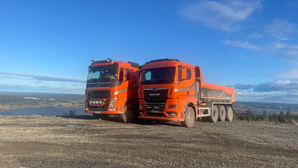 To røde lastebiler parkert på anleggsområde