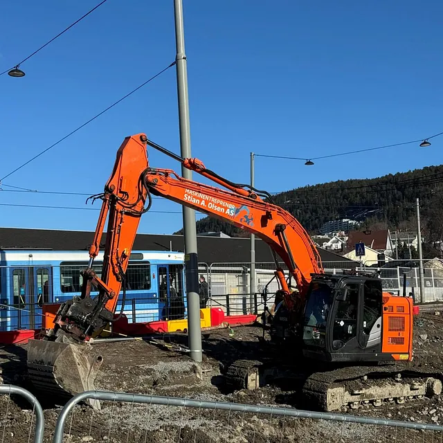 Gravemaskin fra Stian A. Olsen AS arbeider på anleggsområde ved trikkelinje i bymiljø.