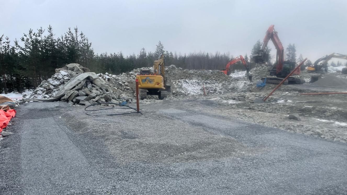 Opparbeidet anleggsområde med gravemaskiner og steinmasser i tåkete vær
