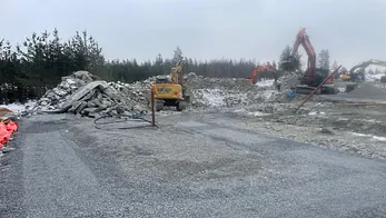 Opparbeidet anleggsområde med gravemaskiner og steinmasser i tåkete vær