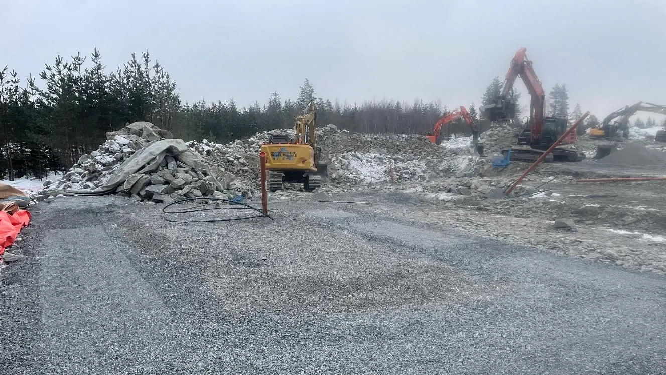 Opparbeidet anleggsområde med gravemaskiner og steinmasser i tåkete vær