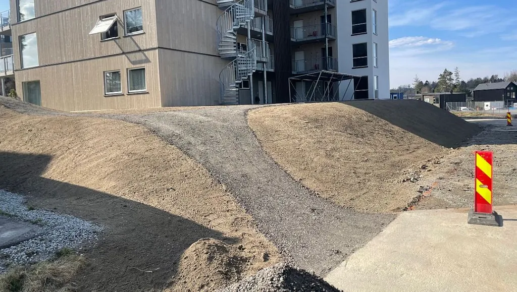 Nytt leilighetsbygg omgitt av gruslagte skråninger og adkomstvei.