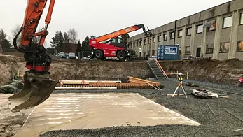 Gruslagt byggegrop med armeringsjern, gravemaskin og teleskoplaster bak.