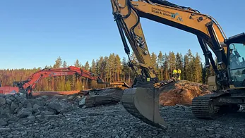 To gravemaskiner arbeider med stein og masser i solbelyst anlegg