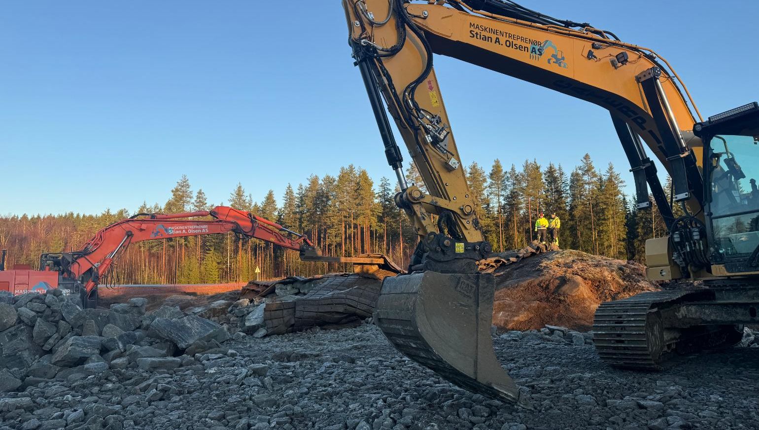 To gravemaskiner arbeider med stein og masser i solbelyst anlegg