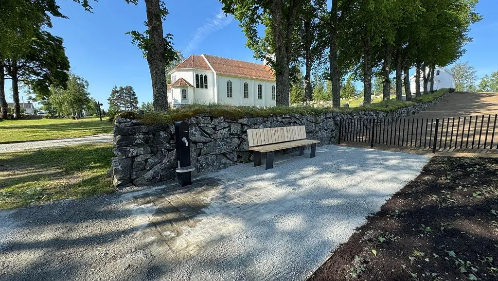 Svart vannpost og benk på kirkeområde